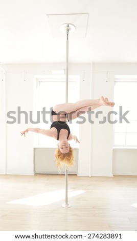 female pole dancer holding a pole with both hands and her body perpendicular to the pole with one leg stretched and one leg bent backwards