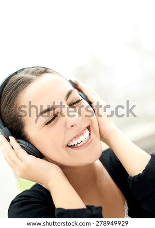 Vivacious young woman enjoying her music laughing as she holds her headphones to her ears, close up of her face with her eyes closed in bliss