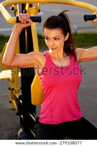 Above view of woman looking sideways smiling while exercising arms on weights machine.