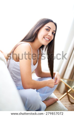 Side view of woman sitting on couch smiling and playing with hair.