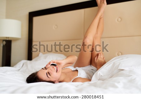 Woman lying upside down in bed, legs resting against headboard and talking on cell phone.