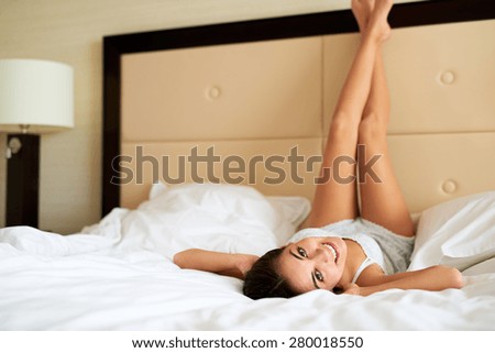 Attractive woman lying upside down in bed smiling with legs resting against headboard.