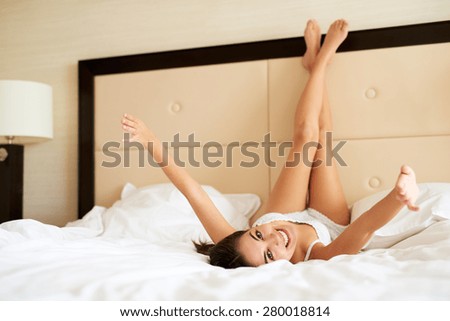 Attractive woman lying upside down smiling with legs resting against headboard and arms stretched out.