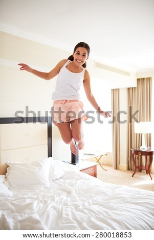 Attractive woman smiling jumping on the bed looking at the camera.