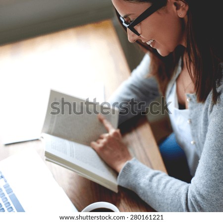 Woman sitting at desk  taking a break from work reading a book.