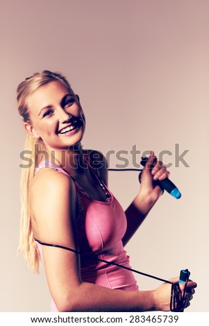 healthy woman smiling at camera and holding a jump rope around her back.