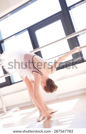 Young Ballerina Wearing Pink Tutu Stretching in First Position at Barre in Sunny Dance Studio
