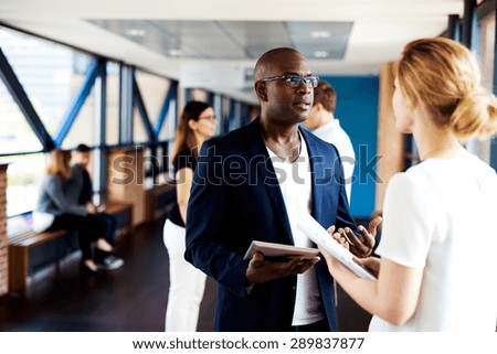 Black male executive standing and talking to white female colleague holding notepads