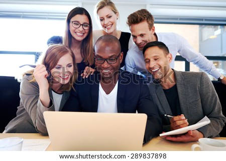 Group of executives smiling and gathered together looking at laptop