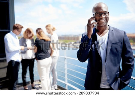 Black male executive smiling holding cellphone to ear and standing with hand in pocket