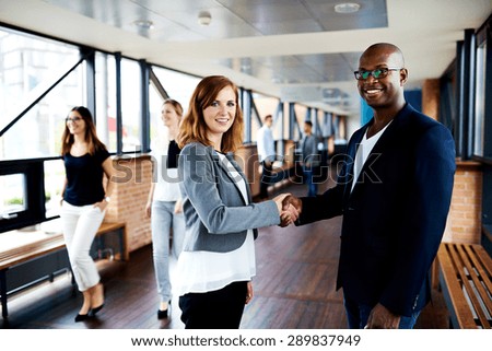 White female executive and black male executive shaking hands in hallway and smiling at camera