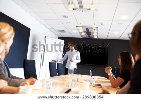 White male executive leading a meeting and pointing to a whiteboard in a conference room