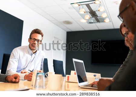 Young white male executive smiling at camera during work meeting.