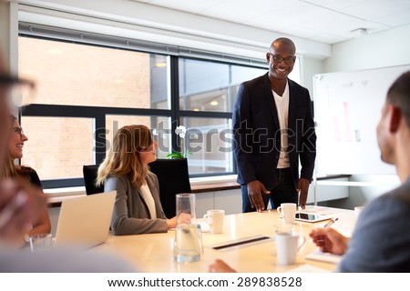 Black male executive standing and leading a work meeting in conference room