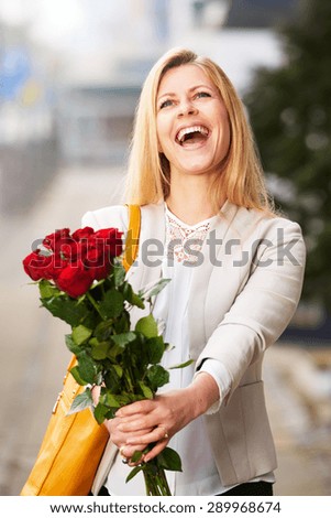 White woman grinning with head tilted back and holding a bouquet of red roses