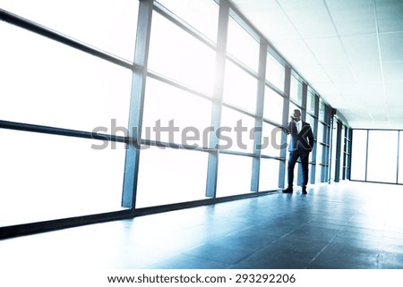 African American Businessman Talking To Someone on Mobile Phone While Leaning on Glass Window Inside a Building.