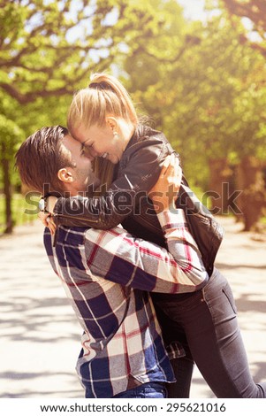 Loving couple having fun in the park as the man lifts his girlfriend, wife or partner into the air so that their foreheads touch, both are smiling and looking into each others eyes with emotion
