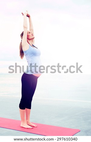 Pregnant woman doing aerobics exercises to improve her breathing for childbirth standing on an exercise mat stretching her arms above her head