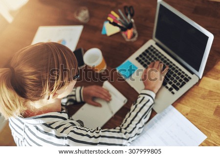 Young female entrepreneur working sitting at a desk typing on her laptop computer in a home office, view from above