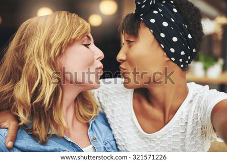 Playful teasing attractive young women friends puckering up for a kiss as they face each other in an intimate embrace with a look of amusement on their faces