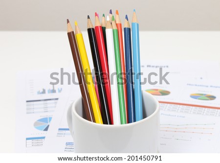 image of color pencils in coffee cup on business paper and desk