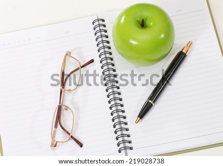 image of book with pen glasses and green apple on desk