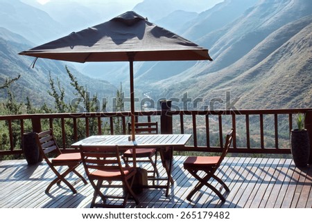 Table and chairs under umbrella on terrace against blue mountains. Shot in Tsehlanyane Nature Reserve, Lesotho.