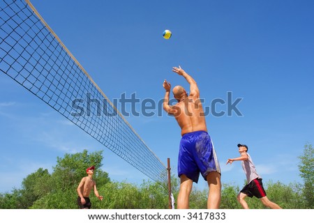 People playing beach volleyball - balding man passes the ball for spike. Shot near Dnieper river, Ukraine.