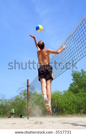 Playing beach volleyball - short balding man hits the ball. Shot near Dnieper river, Ukraine.