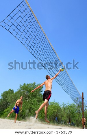 People playing beach volleyball - tall man hits the ball in jump. Shot near Dnieper river, Ukraine.