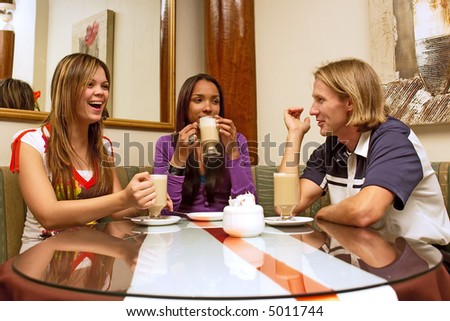 Three friends are drinking coffee in a restaurant with mirrors on wall. Shot in Western Cape, South Africa.