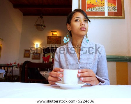 Black asian girl waits in cafe (focus on face). Shot in Western Cape, South Africa.