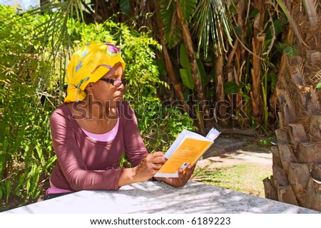 African woman reads book in shadow of a palm. Shot in the Botanical Garden, Stellenbosch, Western Cape, South Africa.