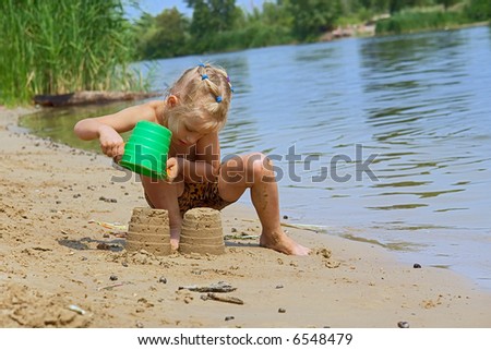 Girl plays with scoop and bucket of sand on beach. Shot in July, Dniepropetrovsk, Ukraine.