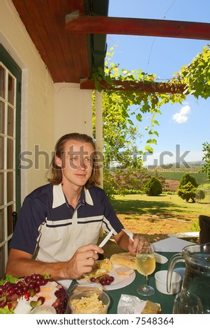 Friendly man dreams/thinks while dining in outdoor winefarm restaurant among awesome mountains (focus on face). Shot near Stellenbosch, Western Cape, South Africa.