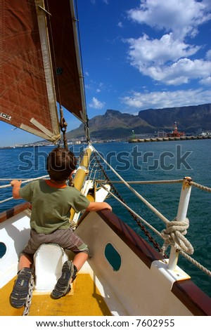 Boy on red-sail yacht\'s desk heading towards Table Mountain. Shot during yacht cruise in Waterfront, Cape Town, South Africa.
