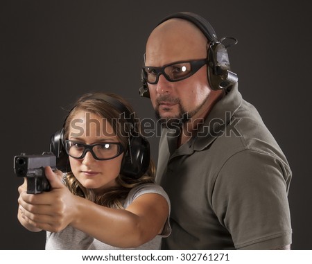 PERSONAL DEFENSE, GUN SAFETY | Young woman learning proper gun control and weapon safety with instructor, wearing safety glasses and ear protection.  Her finger is straight and off the trigger.