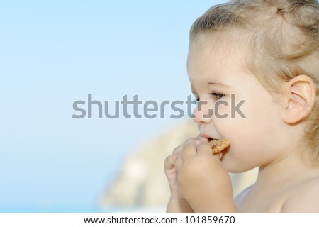 Happy child on the beach eating her snack cake, summer vacation concept