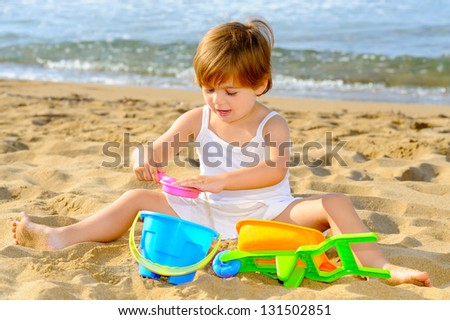 Smiling toddler girl playing with her toys at beach
