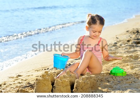 Smiling toddler girl playing with her toys at beach