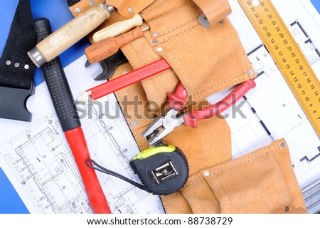 Different carpenter tools: saw, hummer, tape measure, level ruler, screwdriver are lying  upon the blueprints and drawings