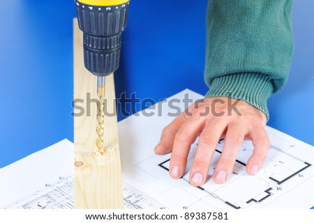 Croped carpenter`s hand with blueprints and drill machine
