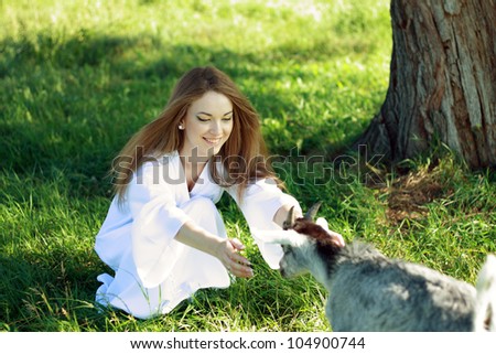 young beautiful smiling woman outdoors pulling her hands to the little goat limb. Looks like a forest fairy