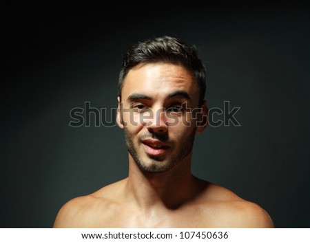 portrait of topless macho man raising his eyebrow and smiling over black background