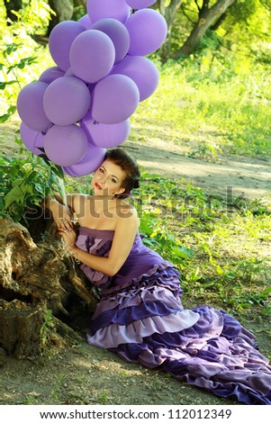 fashion beautiful young woman outdoors in the park with baloons in violet dress and violet baloons in her hand