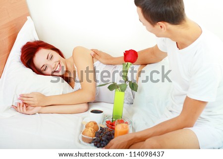 Man serves the breakfast  in bed  to his wife and awaking her. high key light. focus on woman
