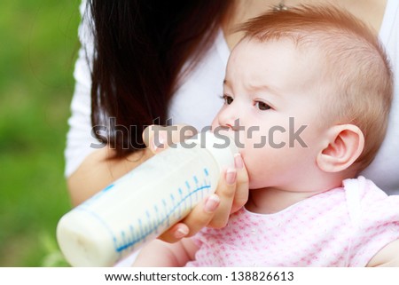 Beautiful young mother is feeding her baby from a bottle outdoor