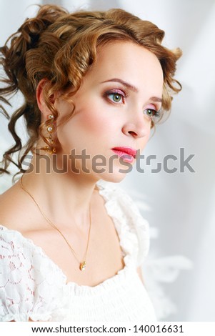 Beautiful woman with romantic bride hairstyle wearing in white wedding dress posing in interior apartment