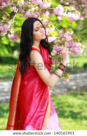 beautiful asian indian woman in the park on a warm spring day with blossom flowers around her