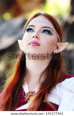 Elf warrior girl on the rock in red cloak posing outdoor close up face